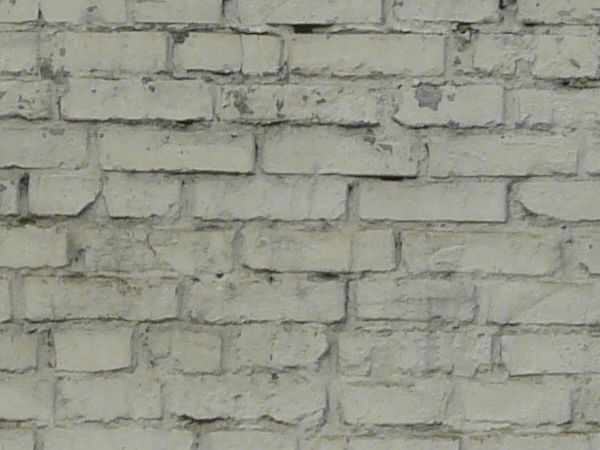 Brick fence texture made up of bricks painted white, with two tall columns made up of similar bricks. Bricks are in various degrees of relief and states of erosion.